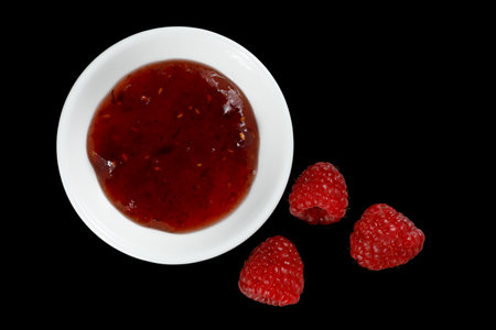 raspberries and jam on black. Jar with delicious raspberry jamの写真素材