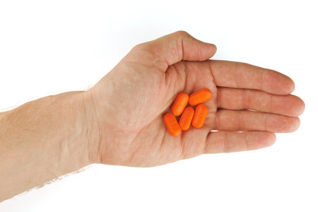 Orange oblong tablet in the palm isolated on whiteの写真素材