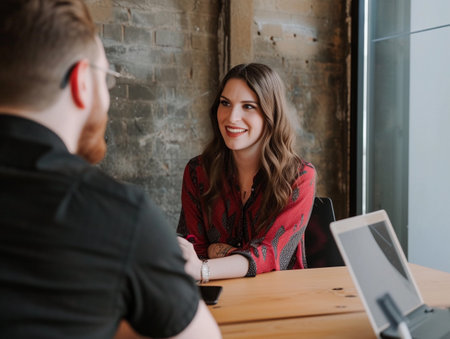 A smiling woman listens intently across a table in an office setting.の素材