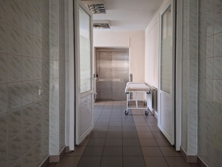 A quiet hospital corridor features a wheeled stretcher and soft morning light illuminating sterile walls. The space conveys a sense of calm.の写真素材