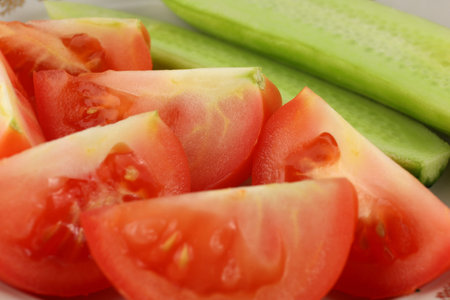Juicy red tomatoes and crisp cucumbers are artistically arranged on a white plate, showing a fresh and healthy meal option in a kitchen atmosphere.の写真素材