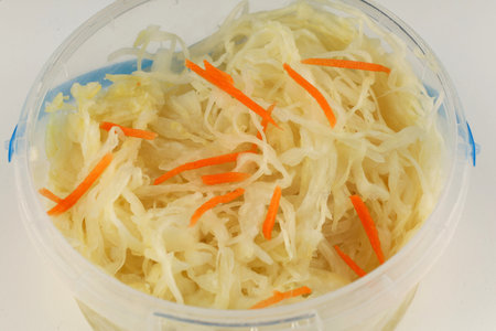 Freshly prepared fermented cabbage mixed with orange carrot strips sits in a clear container, ready...