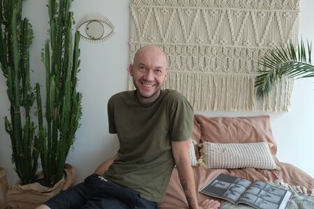 The bald guy in the green shirt sitting on the bed and a smile on his face.の写真素材