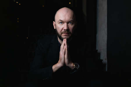 Bald and bearded man is expensively dressed. Man says a prayer