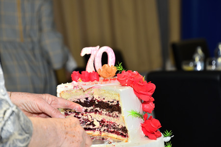 Grandmother slices a large sweet cake with knife at celebrationの写真素材