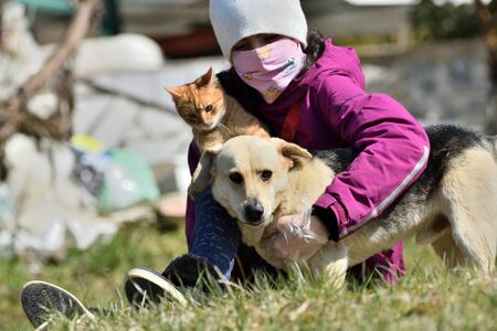Girl with face mask in a hug with domestic dog and cat as a best friends