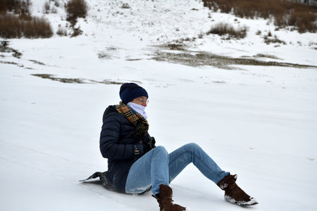 An adult woman sleds down a hill in the winter and brakes with her feet