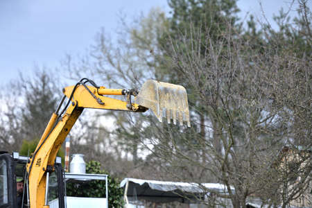 A road excavator digs soil on the foundations of an outbuilding to the house
