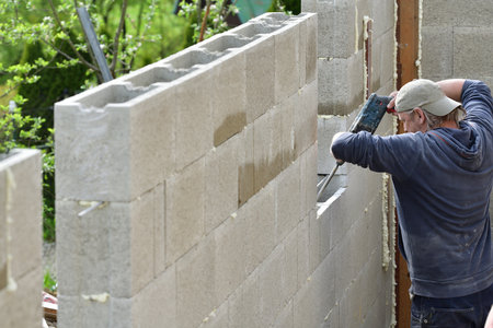Worker building a wall on a house and drilling into a wall with manual drill