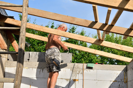 The masons saw wood on the frame under the roof during the construction of the houseの写真素材