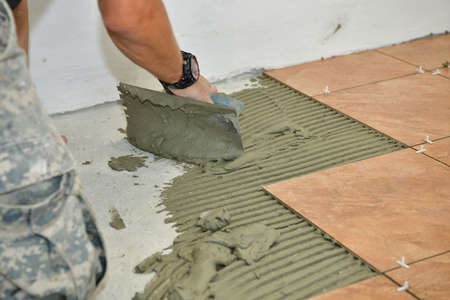 The tiler measures and glues the tiles to the floor of the room