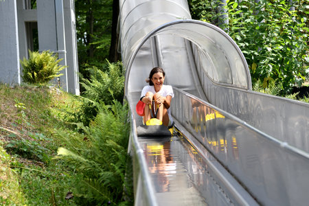 Smiling teenage girl sliding down on toboggan in the summer at an amusement parkの写真素材