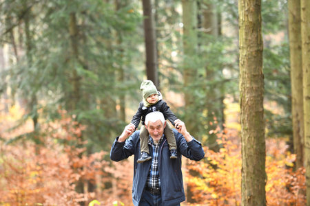 Grandfather carries a little girl on his shoulders during an autumn hike in a colorful forest