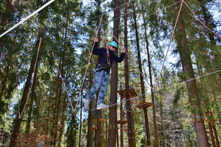 Young man overcomes wooden obstacles at heights holding on to a rope in amusement parkの写真素材