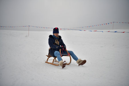 Adult woman sleds down a hill in the winter and brakes with her feetの写真素材