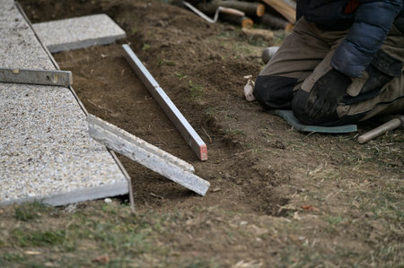 A bricklayer on his knees lays paving around a wooden house