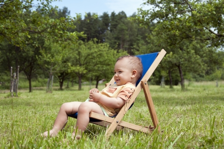 Baby or a toddler child relaxing on a sunbed or a deck chair in a garden の写真素材