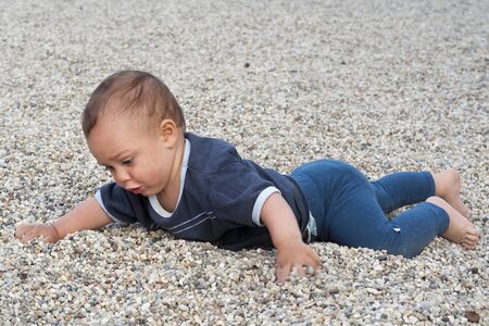 Portrait of a baby or a toddler child, crawling on a pebble  beach and playing with stones and pebbles の写真素材