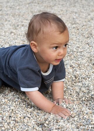 Portrait of a baby or a toddler child, crawling on a pebble  beach and playing with stones and pebbles の写真素材