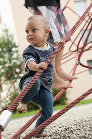 Children, baby toddler and older kid, playing barefoot at playground on a rope climbing frame equipment の写真素材