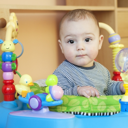 Portrait of a cute 6 month old baby, boy or girl, in a walker of bouncer with attached plastic toys.の写真素材