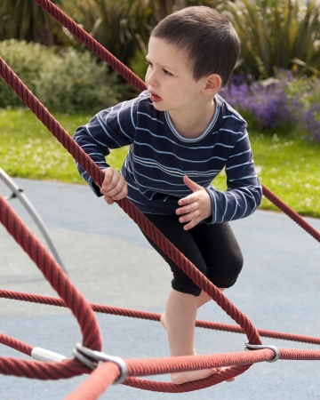 Child playing barefoot at playground on a rope climbing frame equipment の写真素材