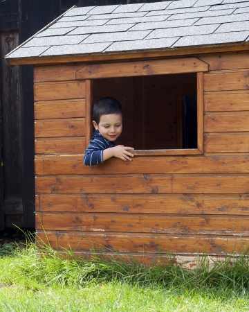 Child boy in a window of a wooden garden shed or play house. の写真素材