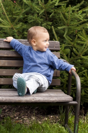 Todller child sitting on wooden bench in a garden or park. の写真素材