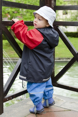 Child toddler in waterproof clothes in a park in rain. の写真素材