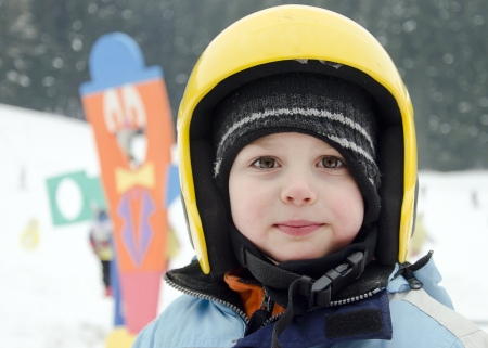 Portrait of a cute child skier, boy or girl, with yellow skiing helmet in a winter ski resort の写真素材