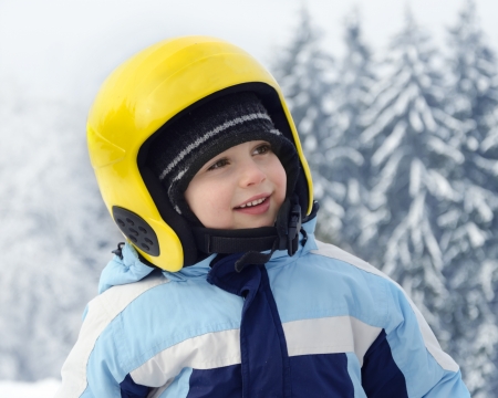Portrait of a cute happy child skier, boy or girl, with yellow skiing helmet in a winter ski resort の写真素材