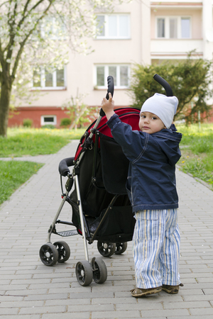 Small child toddler, boy or girl, pushing a stroller on a pedestrian path  の写真素材