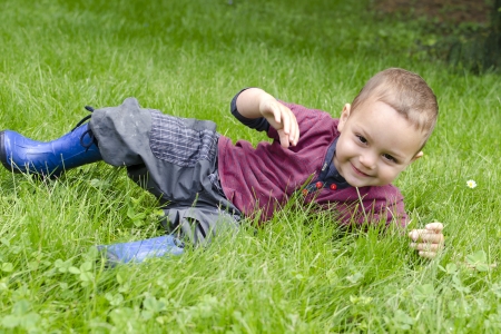 Happy toddler child playing and rolling in grass in garden or meadow の写真素材