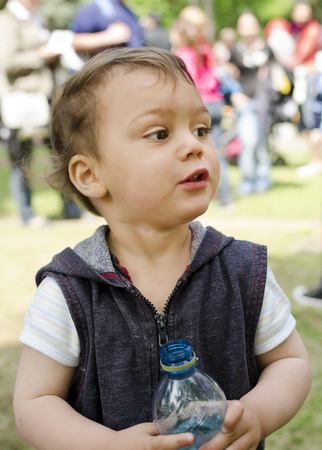 Child holding a plastic water bottle, crowd of festival peopleの写真素材