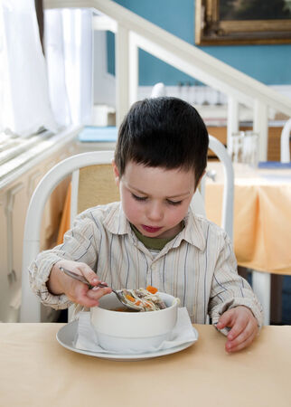 Small child boy eating a soup in a restaurant.の写真素材