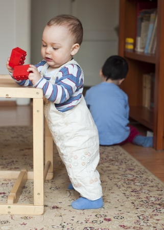 Two children, small toddler or a baby child and his oldrer brother, playing  at home with building blocks.の写真素材