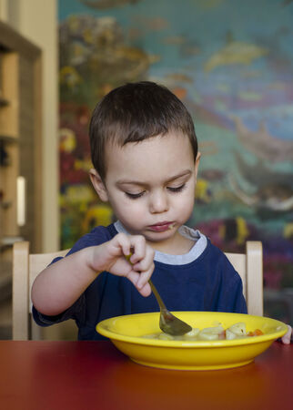 Toddler child eating soup at table at home or at kindergarden  の写真素材