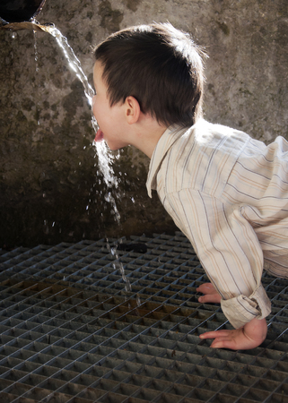 Child drinking water running from and old rustic water pipe fountain; aid concept の写真素材