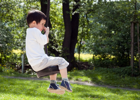 Child boy swinging on a tree swing in an outdoor adventure playground in the park.の写真素材