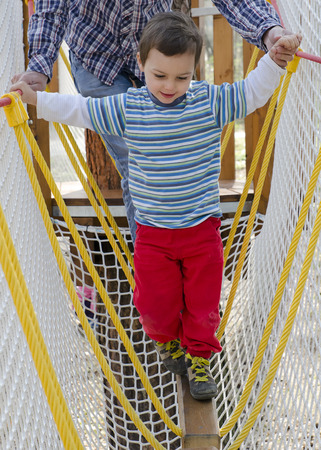 Small child on a obstacle challenge at an advanture playground being helpd by an adult or older child.の写真素材