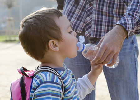 Child drinking water from a platic bottle, his father helping him. の写真素材