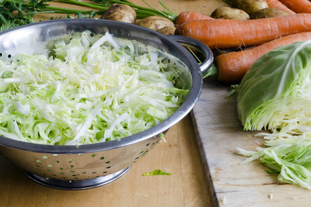 Sliced cabbage in colander and carrot and potatoes on table ready for cooking の写真素材