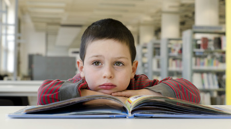 Dreamy child reading book a desk at public library room.の写真素材
