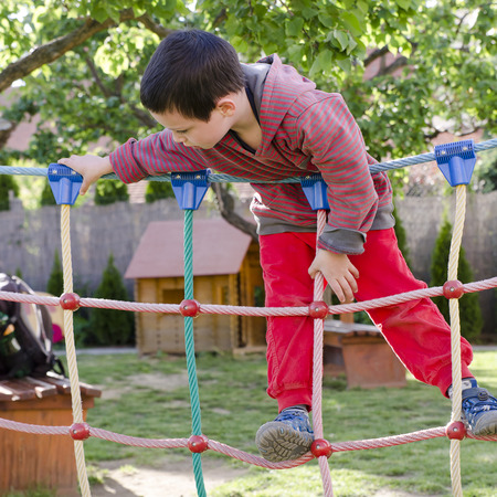 Child palying at children playground, climbing on  rope ladder obstacle course equipment.の写真素材