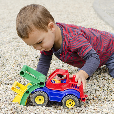 Toddler child boy playing with a plastic toy digger car. 