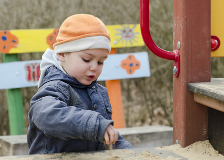 Child toddler, boy or girl,  playing with sand at public playgroundの写真素材