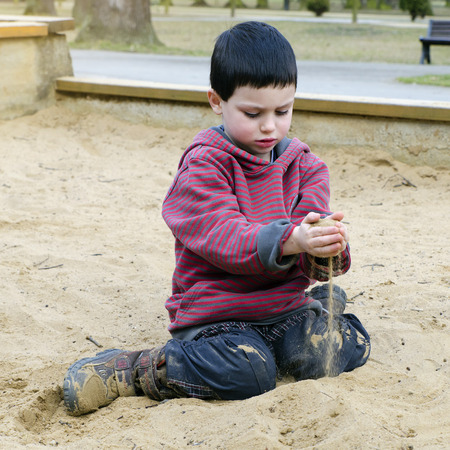 Child toddler, boy or girl,  playing with sand at public playground in a park.の写真素材