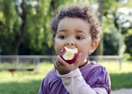 Child girl eating an apple in a park in nature.