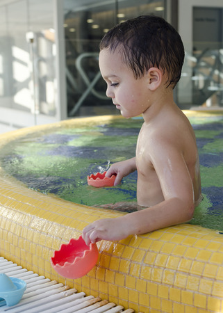 Small child playing in shallow children swimming pool with toys.の写真素材