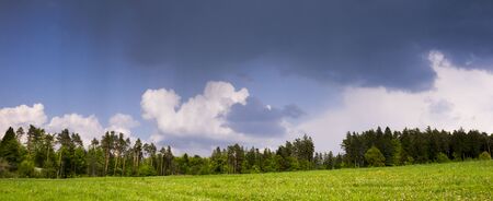 Countryside landscape with rain storm clouds above forest and meadow